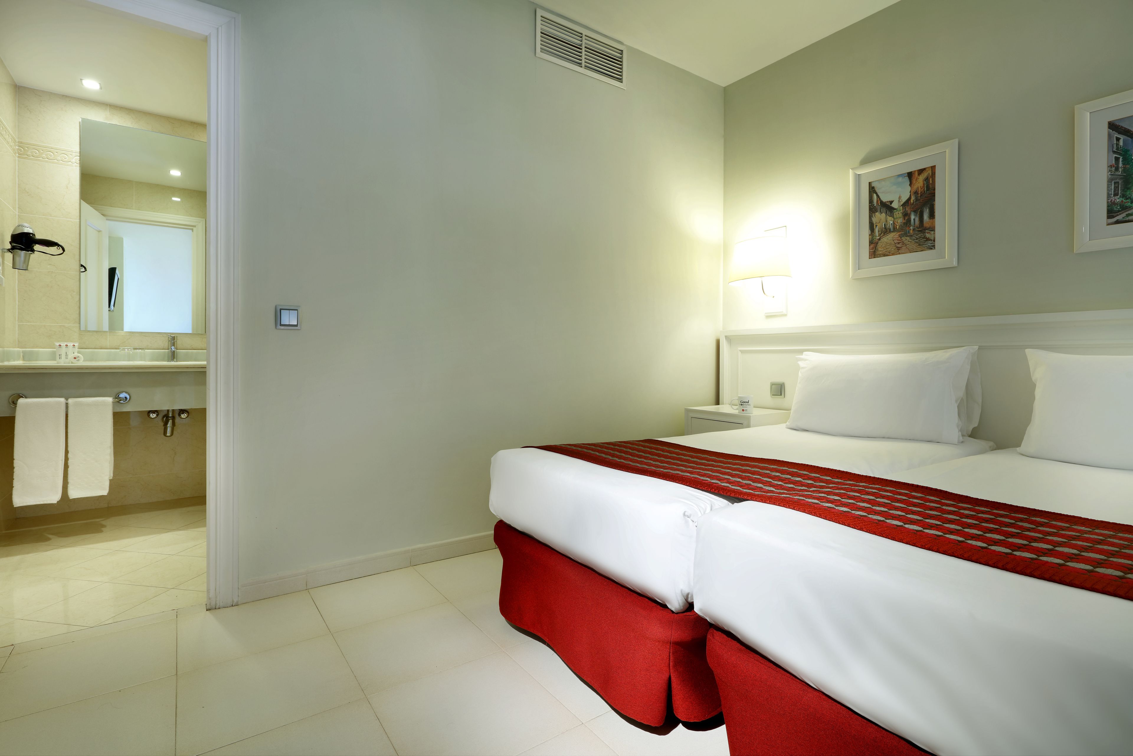 A hotel room with a bed, a bathroom with a mirror, and a painting on the wall.