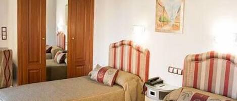Una habitación de hotel con dos camas individuales, una puerta de madera, un cuadro en la pared y una mesita de noche con una lámpara.