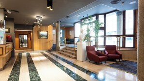 A lobby with marble flooring, red chairs, a staircase, and large windows. - Tibur Hotel (Zaragoza)