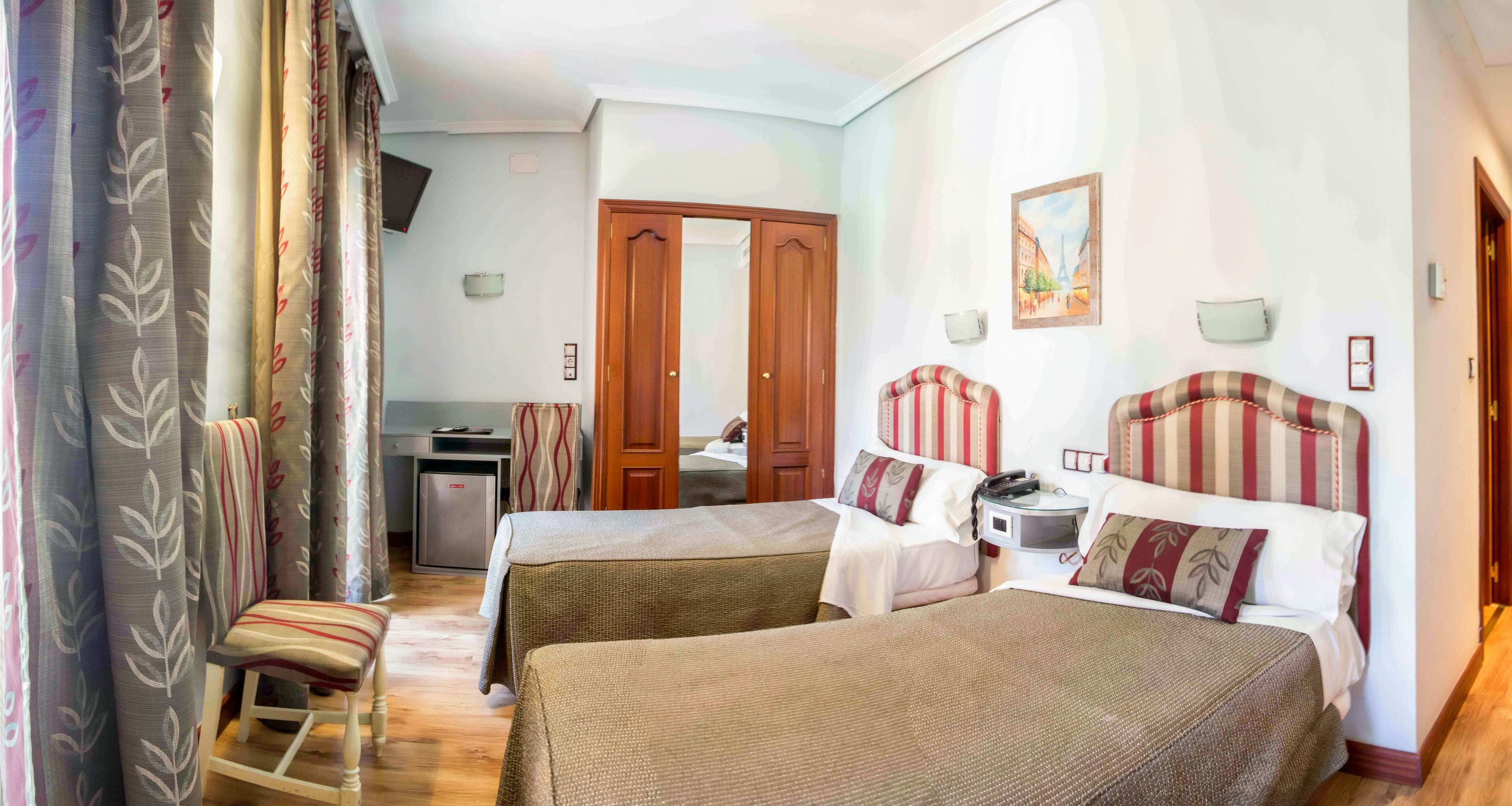 A hotel room with two beds, a desk, a chair, and a wardrobe.
