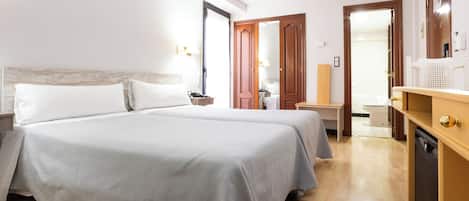 A hotel room with two beds, a wooden floor, a bathroom with a toilet and sink, and a wooden wardrobe.