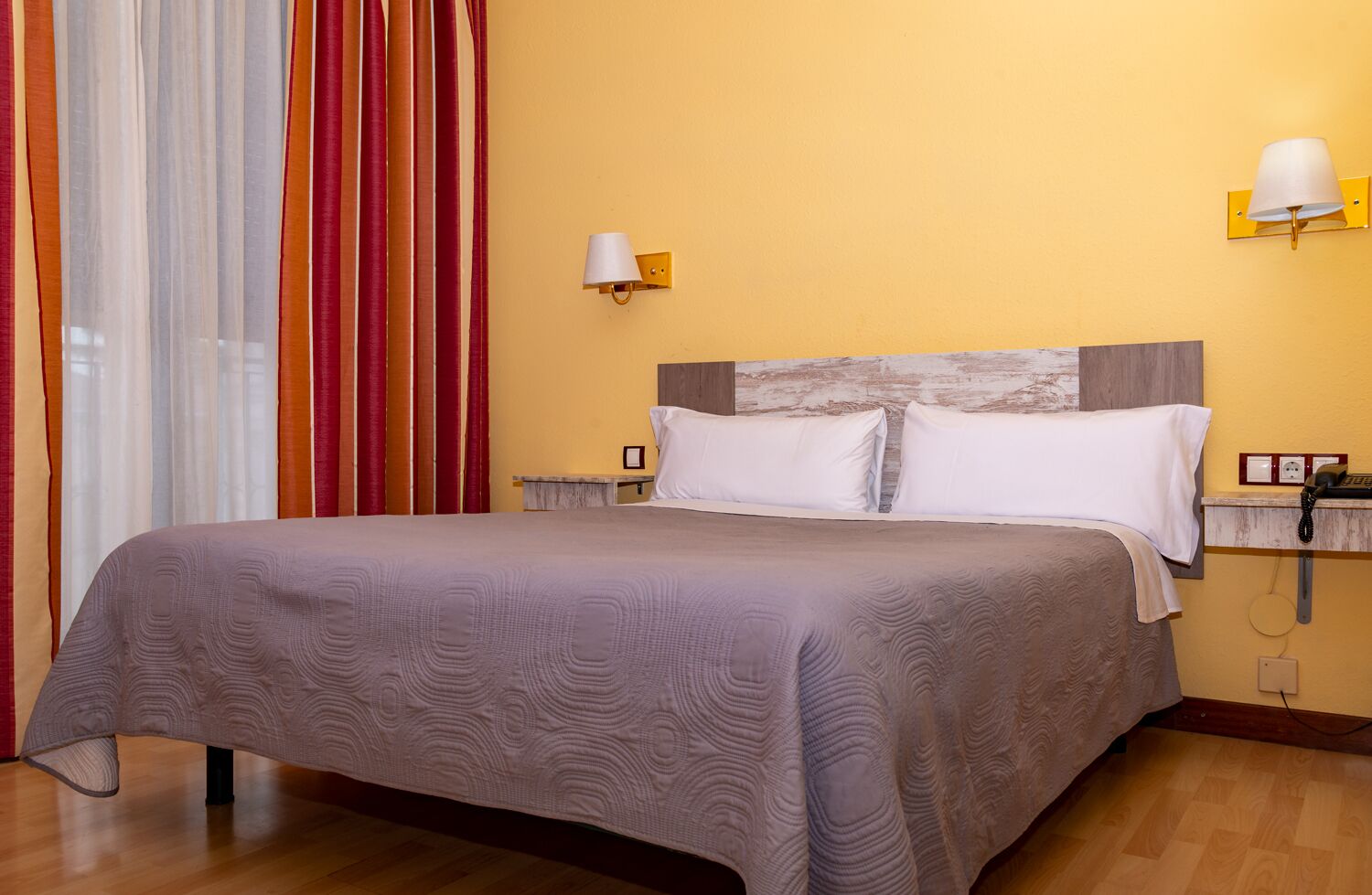 A hotel room with a large bed, two bedside tables, a nightstand, a lamp, and a telephone.