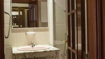Un baño con lavamanos de mármol, un espejo, una ducha y una puerta de madera.