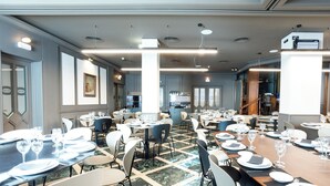 A spacious dining area with multiple tables set for meals, featuring a mix of chairs and a few standing dining options. - Tibur Hotel (Zaragoza)