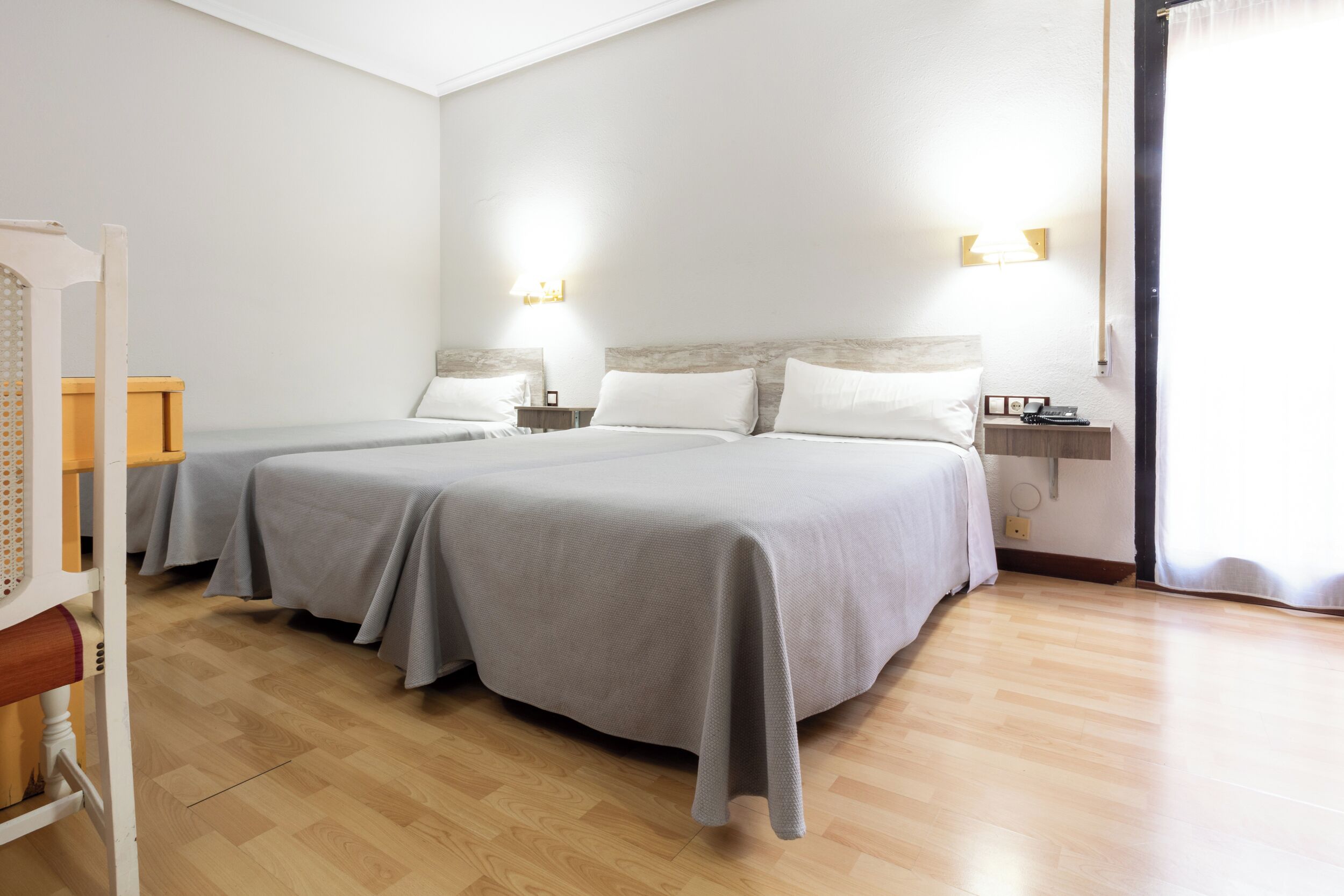A hotel room with two beds, wooden flooring, and bedside lamps.