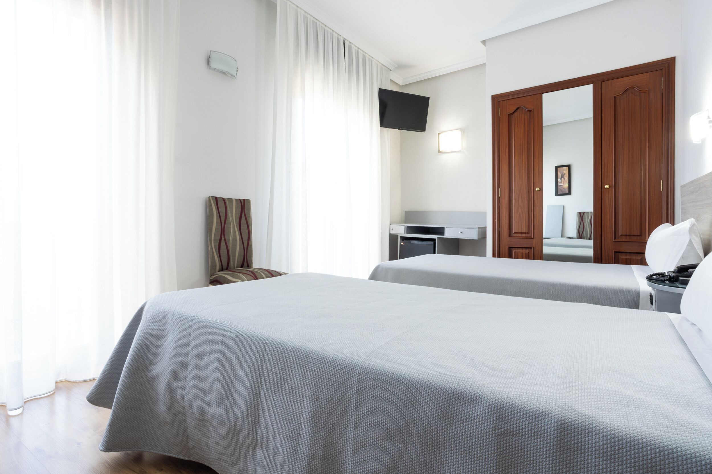 Een hotelkamer met twee bedden, een bureau, een stoel, een televisie en een kledingkast.