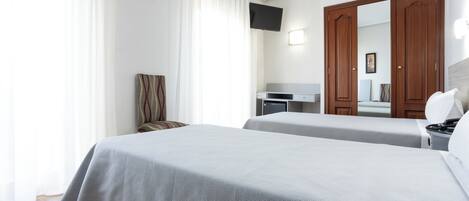 Una habitación de hotel con dos camas, un escritorio, una silla, un televisor y un armario.