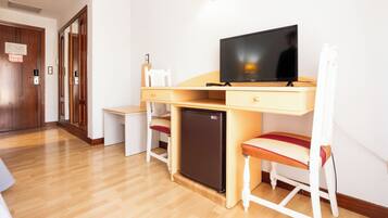 Habitación de hotel con escritorio de madera, televisor, refrigerador minibar y una silla.