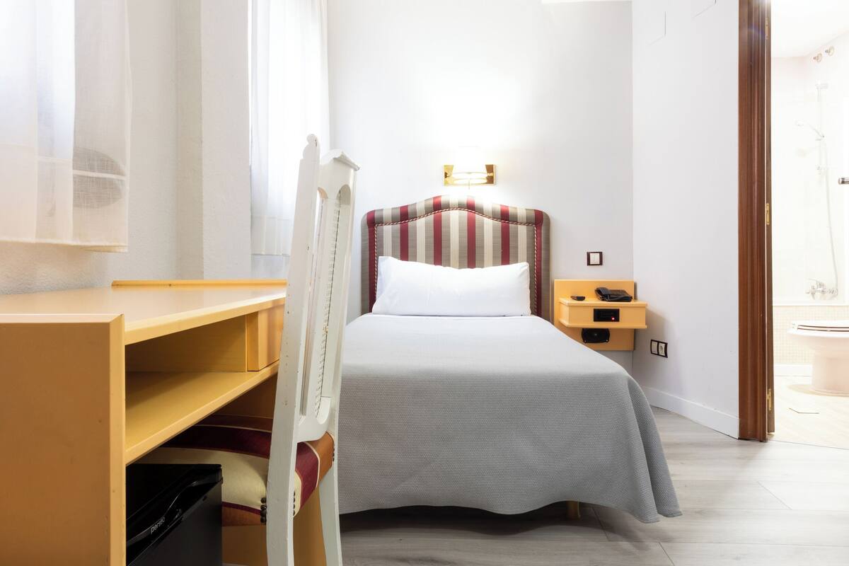A hotel room with a bed, a bedside table, a nightstand, a desk, and a chair.