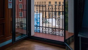 A room with a large glass door leading to a balcony with a view of a historic building with a tower. - Tibur Hotel (Zaragoza)