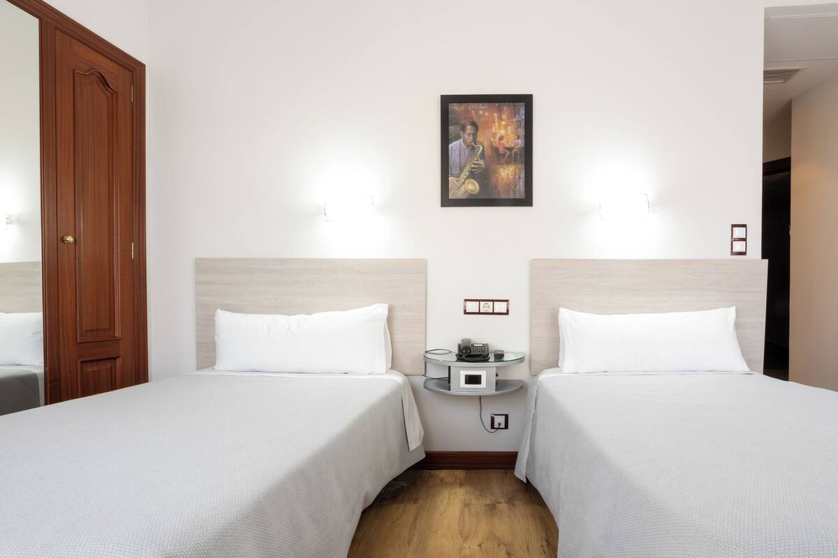 A hotel room with two beds, a wooden door, a wall-mounted picture, and a small table with a radio.