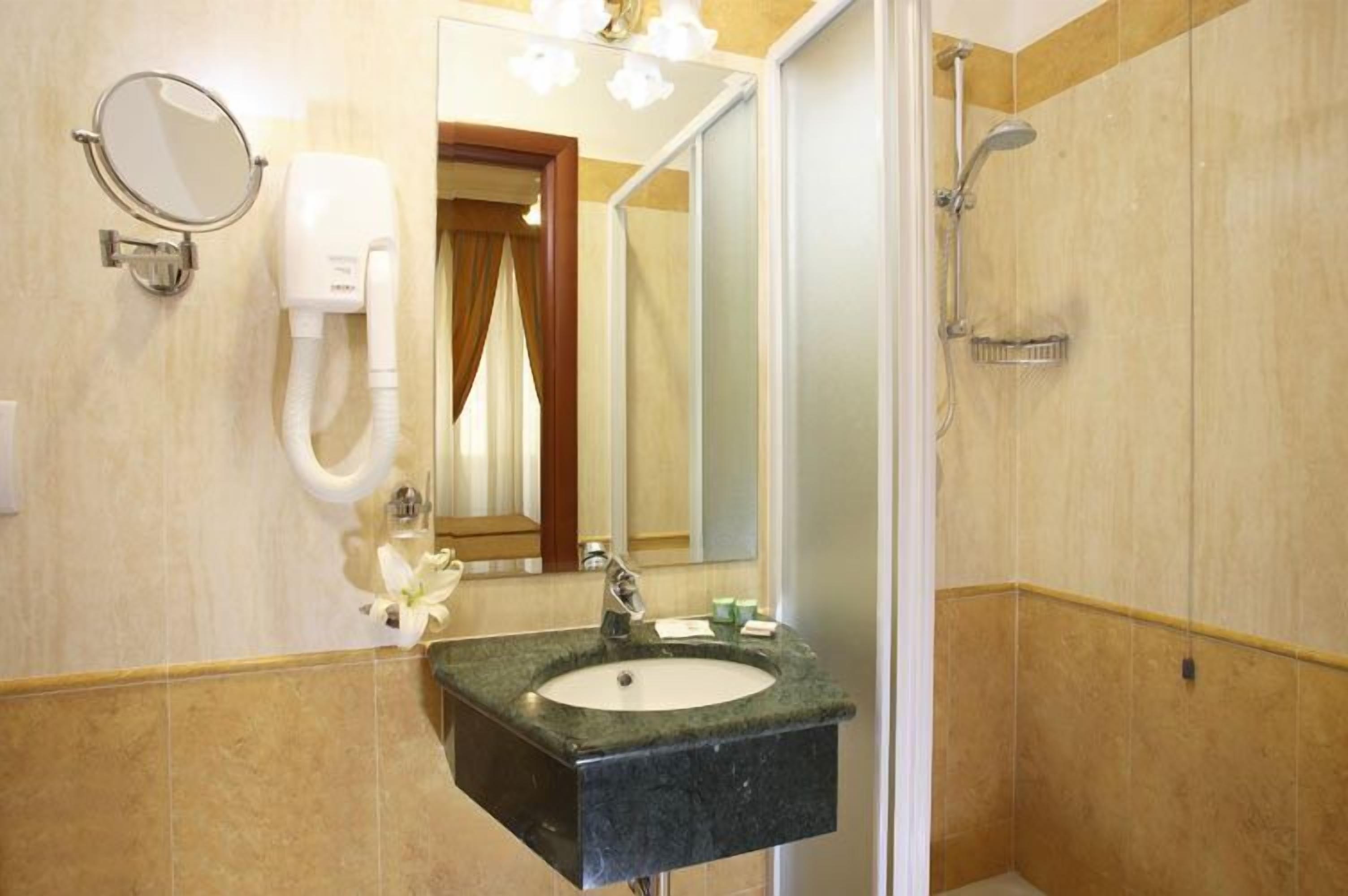 A bathroom with a sink, mirror, hairdryer, and shower.