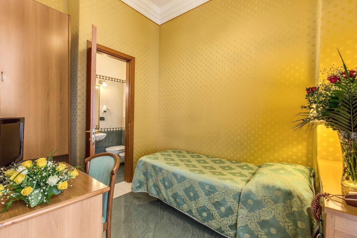 Ein Zimmer mit einem Bett, einem Schreibtisch mit Fernseher und einem durchgegangenen Tür einsehbaren Badezimmer.