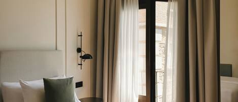 A hotel room with a bed, a bedside table, a lamp, and a window with curtains.