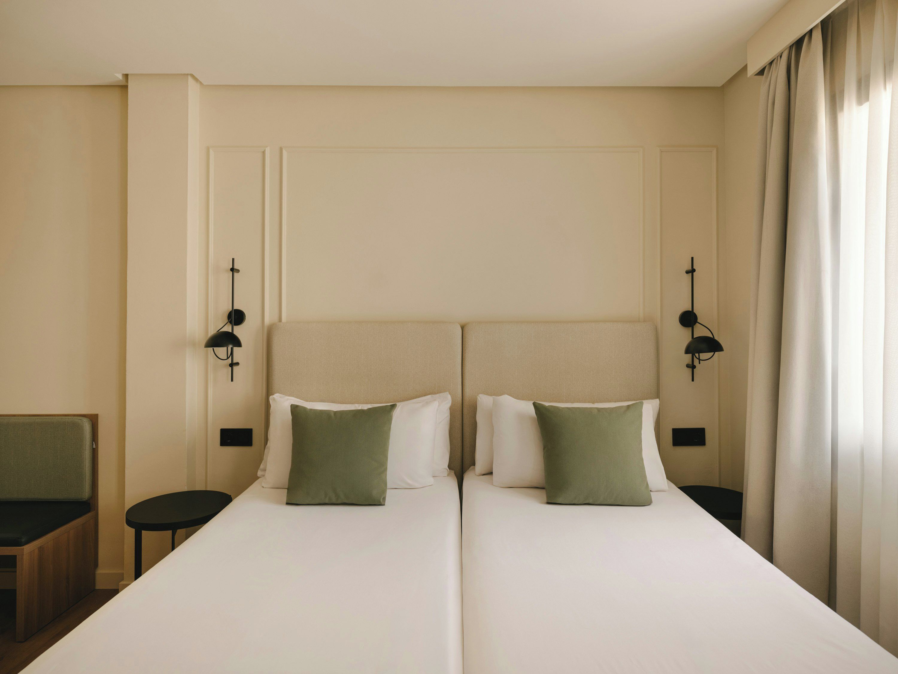 Habitación de hotel con dos camas, una mesita pequeña y dos lámparas de pared.