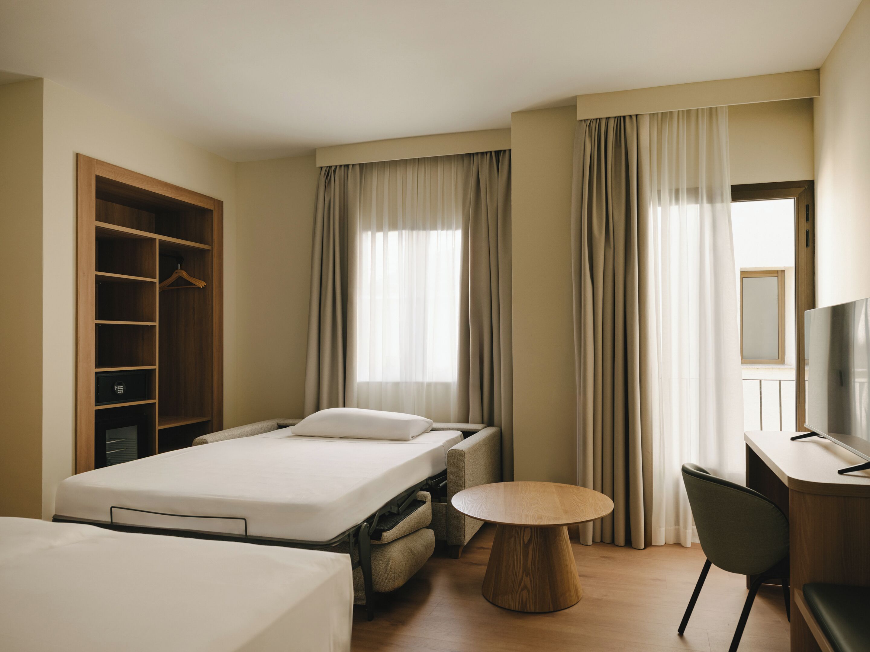 Una habitación de hotel con cama, escritorio, silla, mesa redonda de madera y armario.