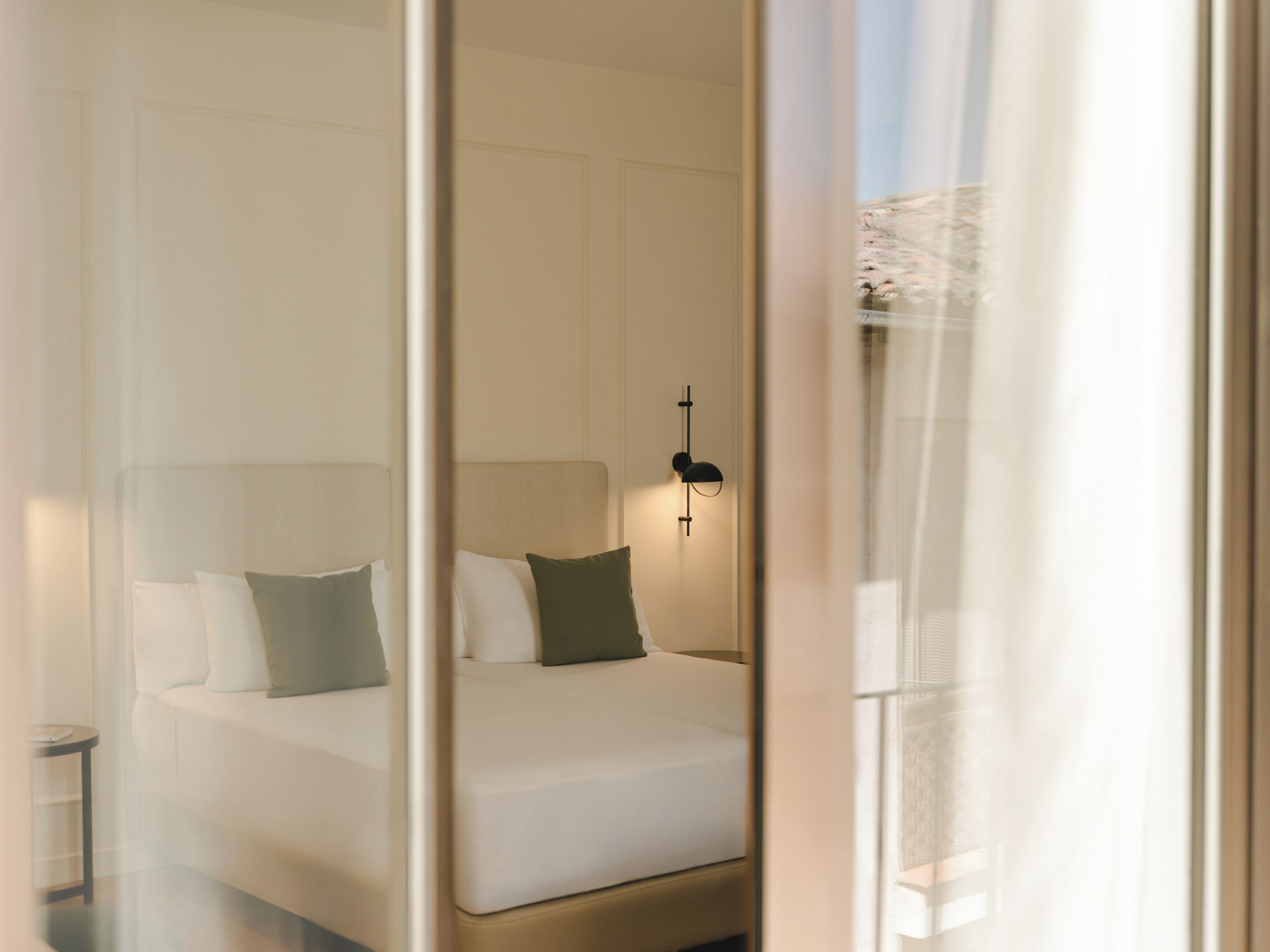 A hotel room with a bed, a nightstand, and a wall-mounted light fixture.