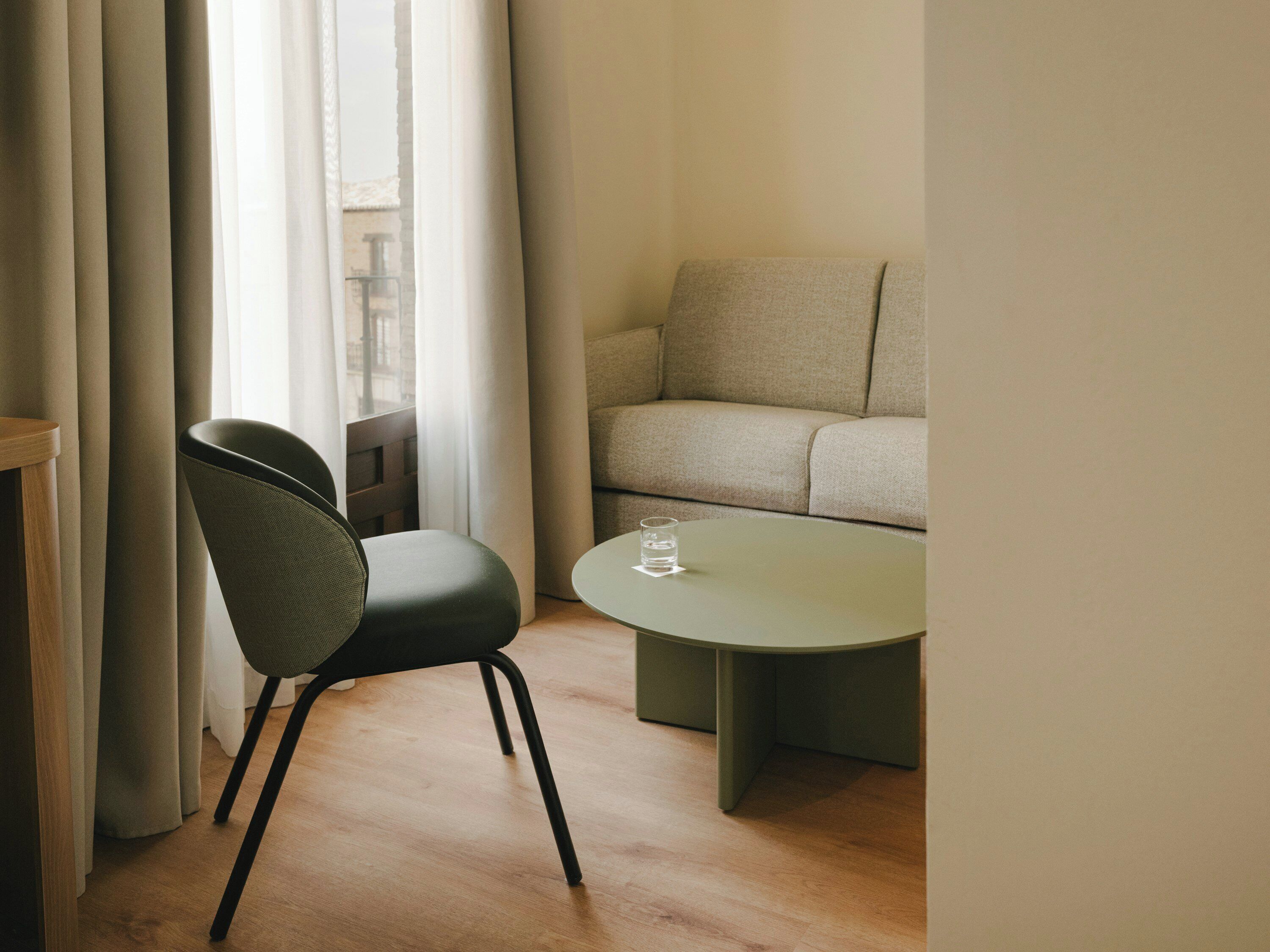 A minimalist room with a sofa, a chair, a round table, and a glass of water.