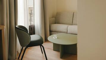 A minimalist room with a sofa, a chair, a round table, and a glass of water.