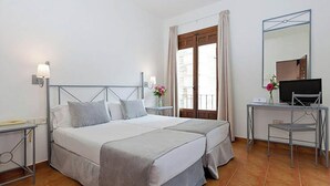 Ein Doppelbett mit Metallgestell, zwei Nachttische mit Lampen, ein Schreibtisch mit Stuhl, ein Fernseher und ein Fenster mit Vorhängen.