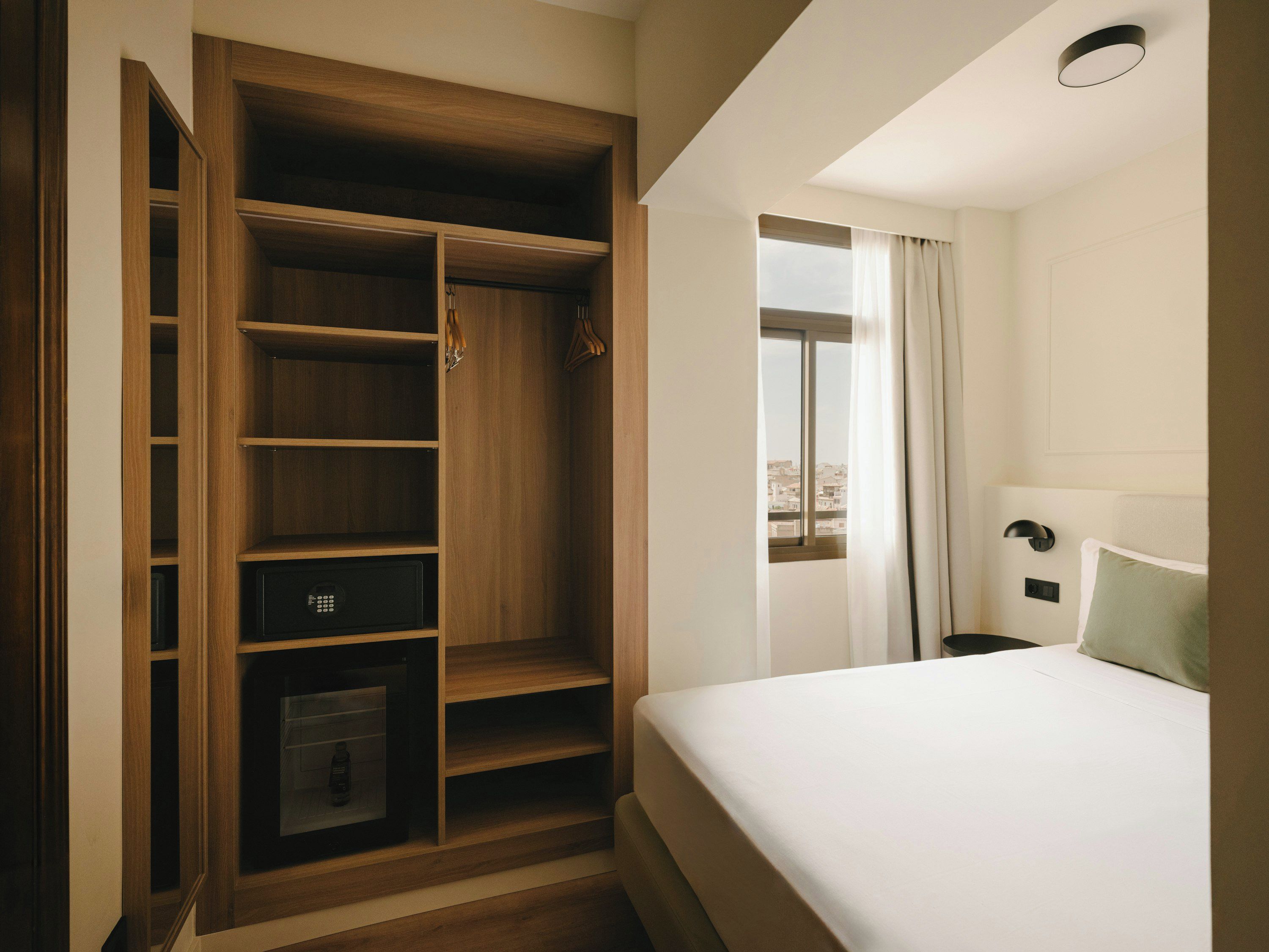 Habitació d'hotel amb un armari gran, un llit, una nit i una finestra amb cortines.