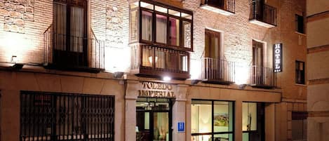 Fachada de hotel con exterior de piedra, varios balcones y una entrada visible con un letrero.