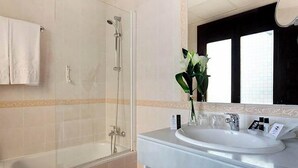 Ein Badezimmer mit einer Duschkabine, einem weißen Waschbecken und einem Spiegel mit dekorativem Rahmen.