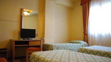 Ein Hotelzimmer mit Schreibtisch, Fernseher, zwei Betten und einem Fenster mit Vorhängen.