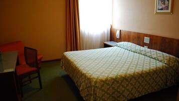 Una habitación de hotel con cama, escritorio, silla y ventana con cortinas.
