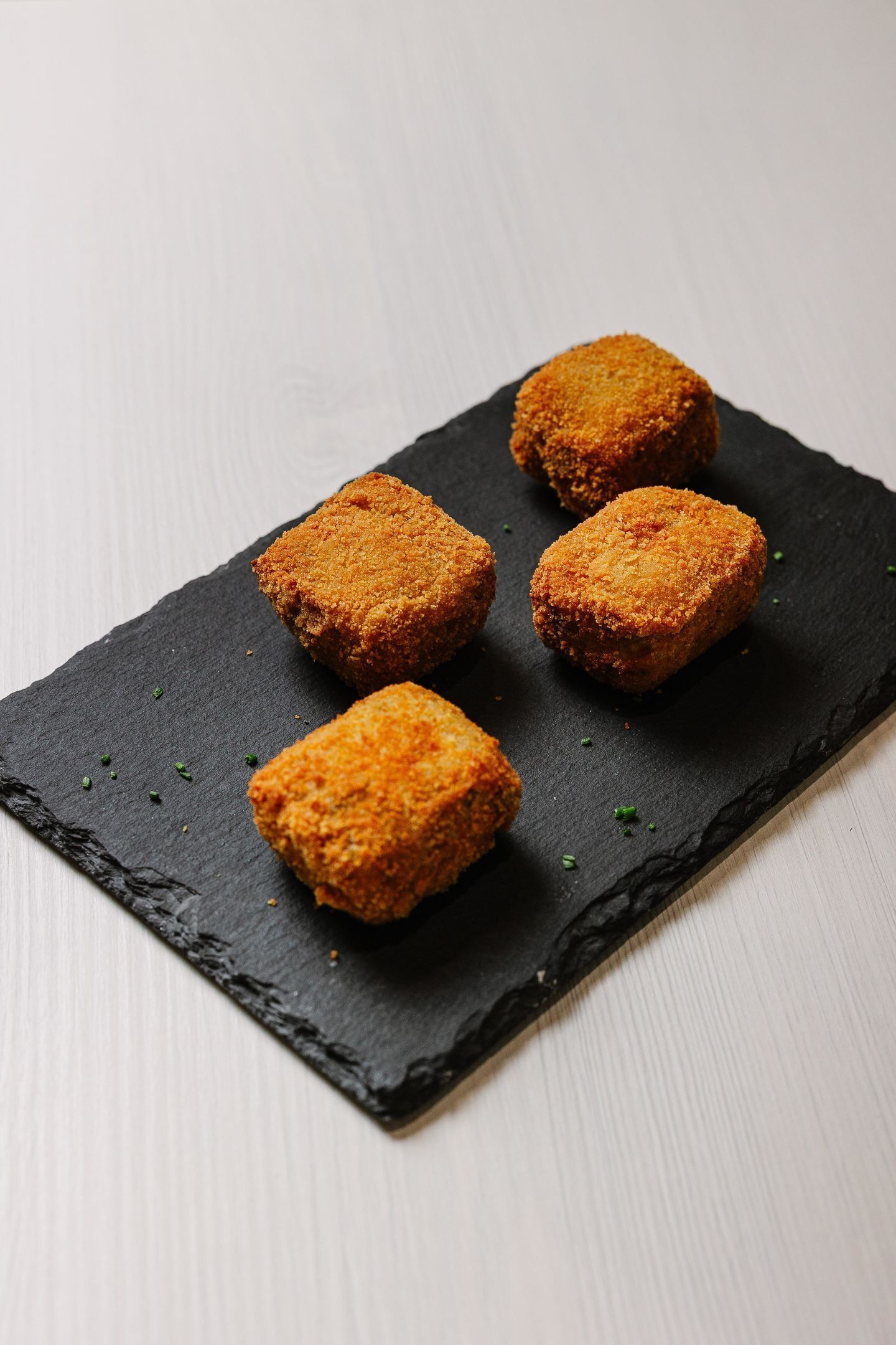 Quatro pratos empanados e fritos sobre um prato de ardósia preta.