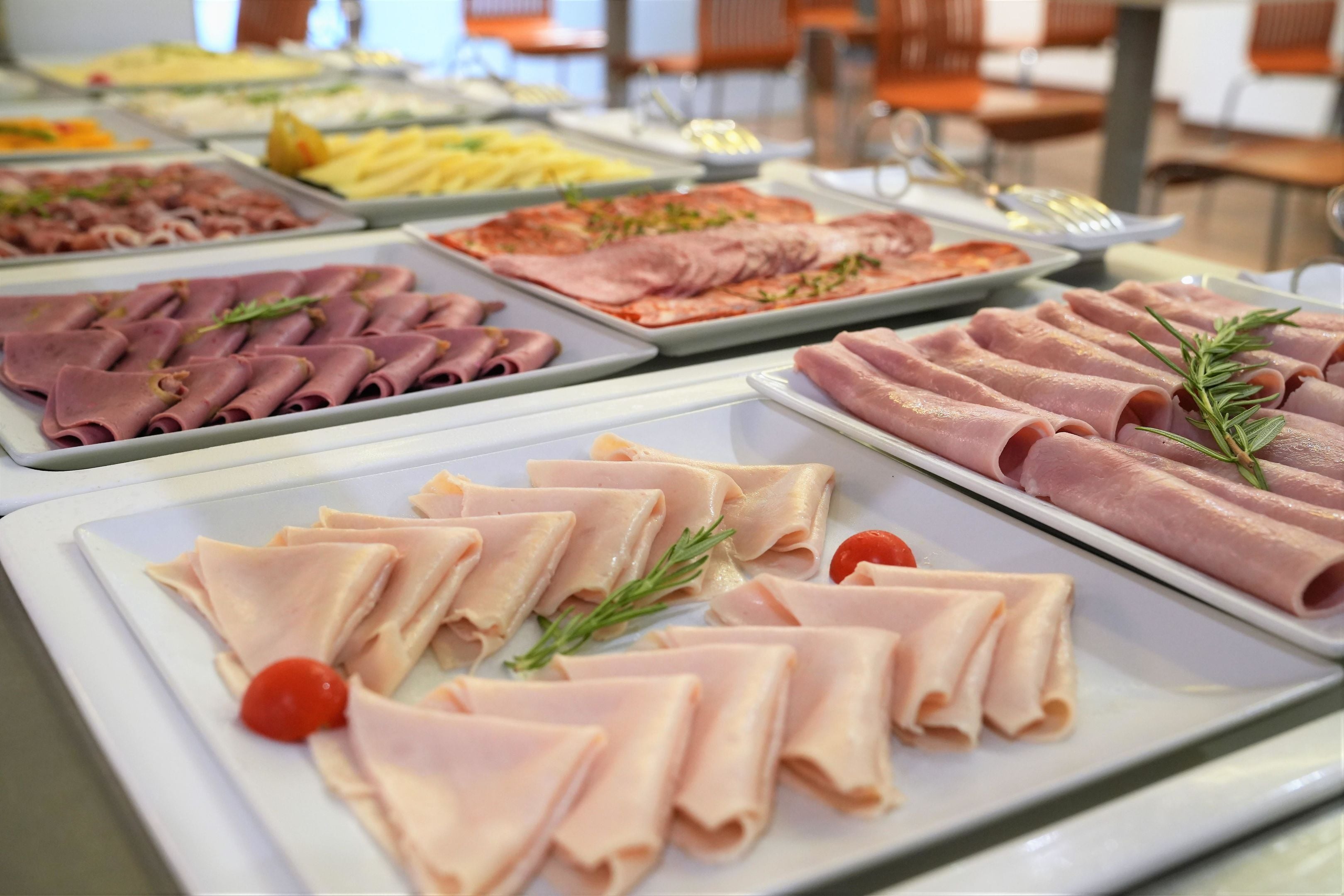Un bufé con diversas fuentes de carne, incluyendo jamón en rodajas y otras opciones, dispuestas en bandejas blancas.