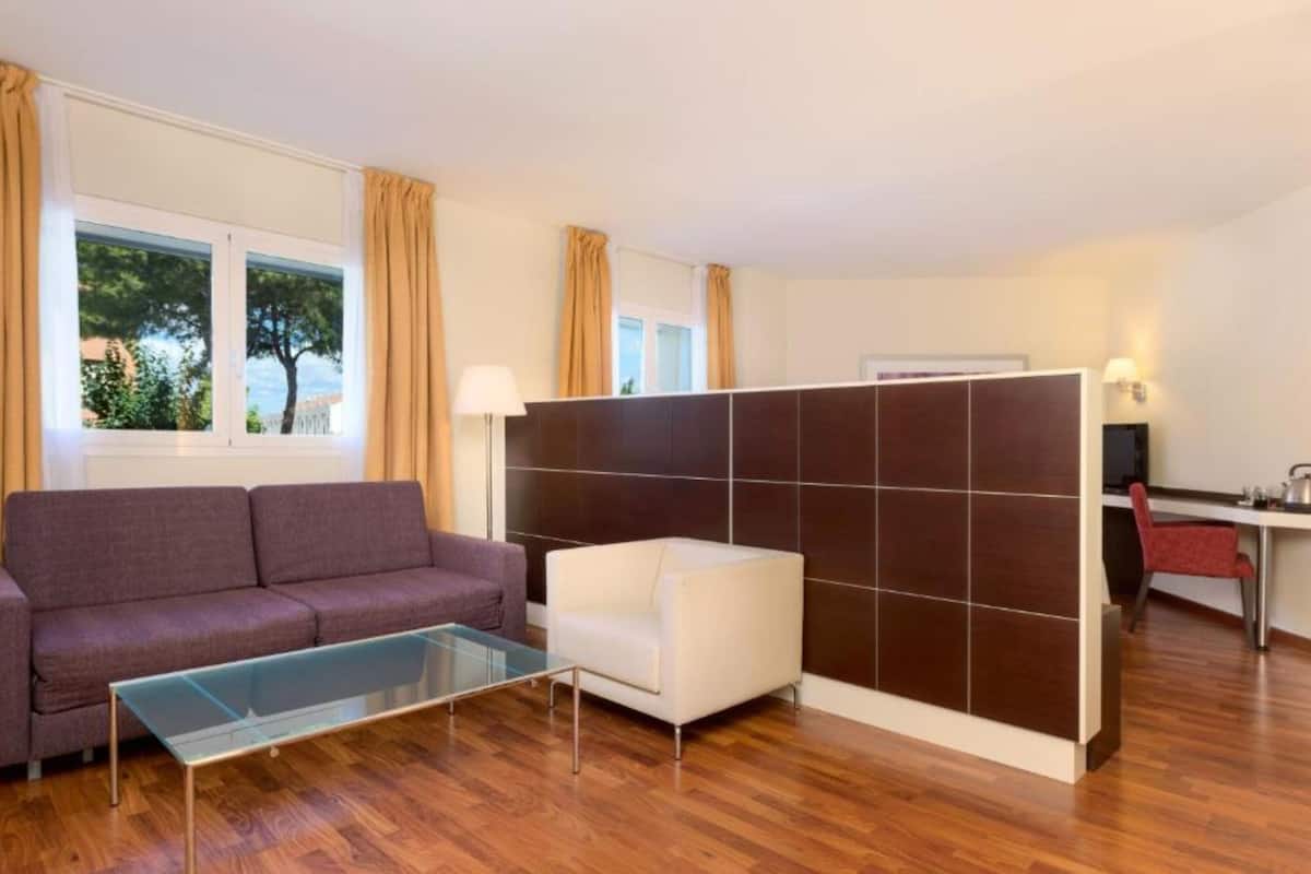 Una sala de estar moderna con un sofá, una mesa de centro de vidrio, un sillón blanco y una pared divisoria.
