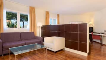 Una sala de estar moderna con un sofá, una mesa de centro de vidrio, un sillón blanco y una pared divisoria.