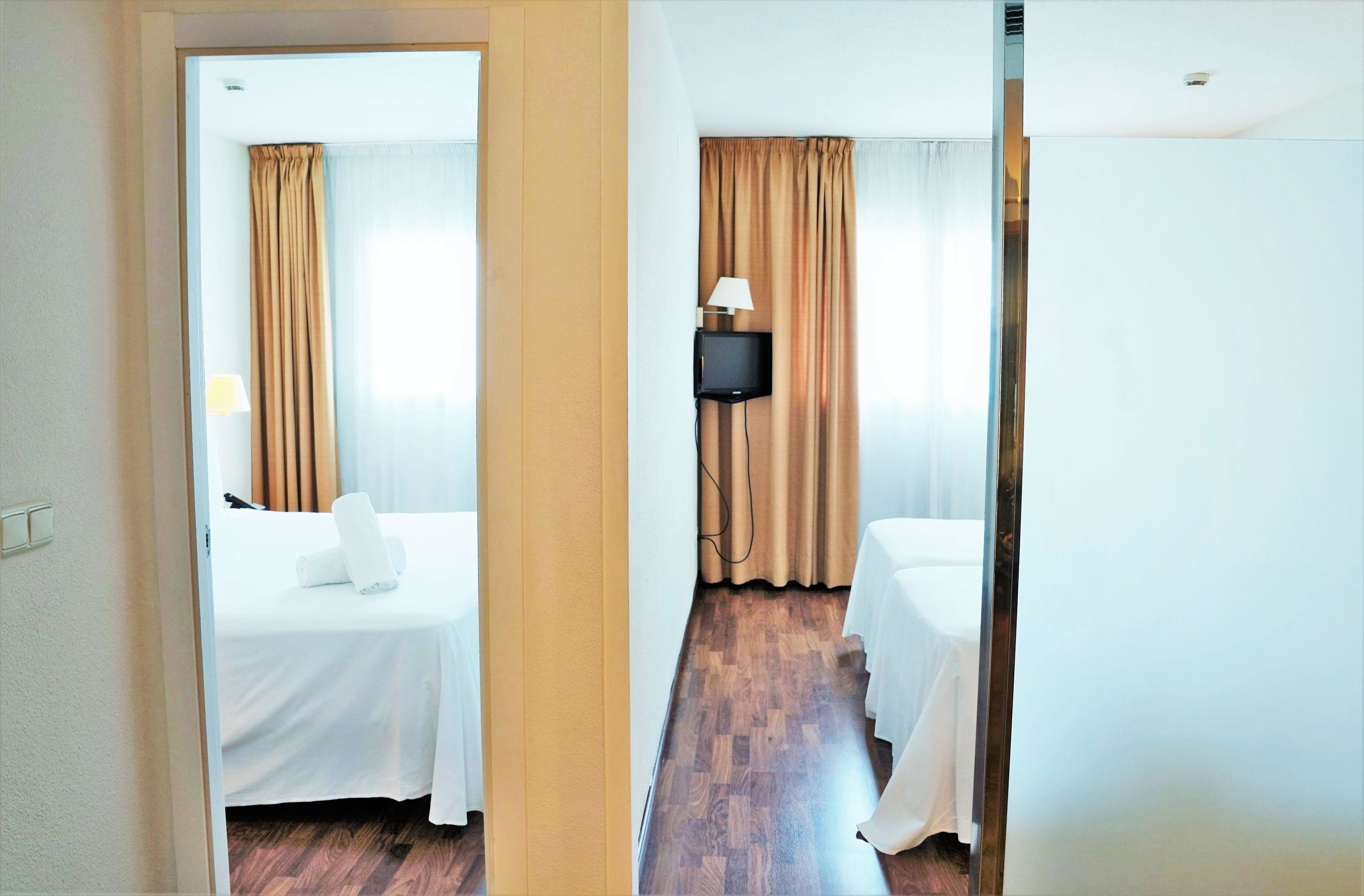 Habitación de hotel con cama, televisor montado en la pared y suelo de madera.