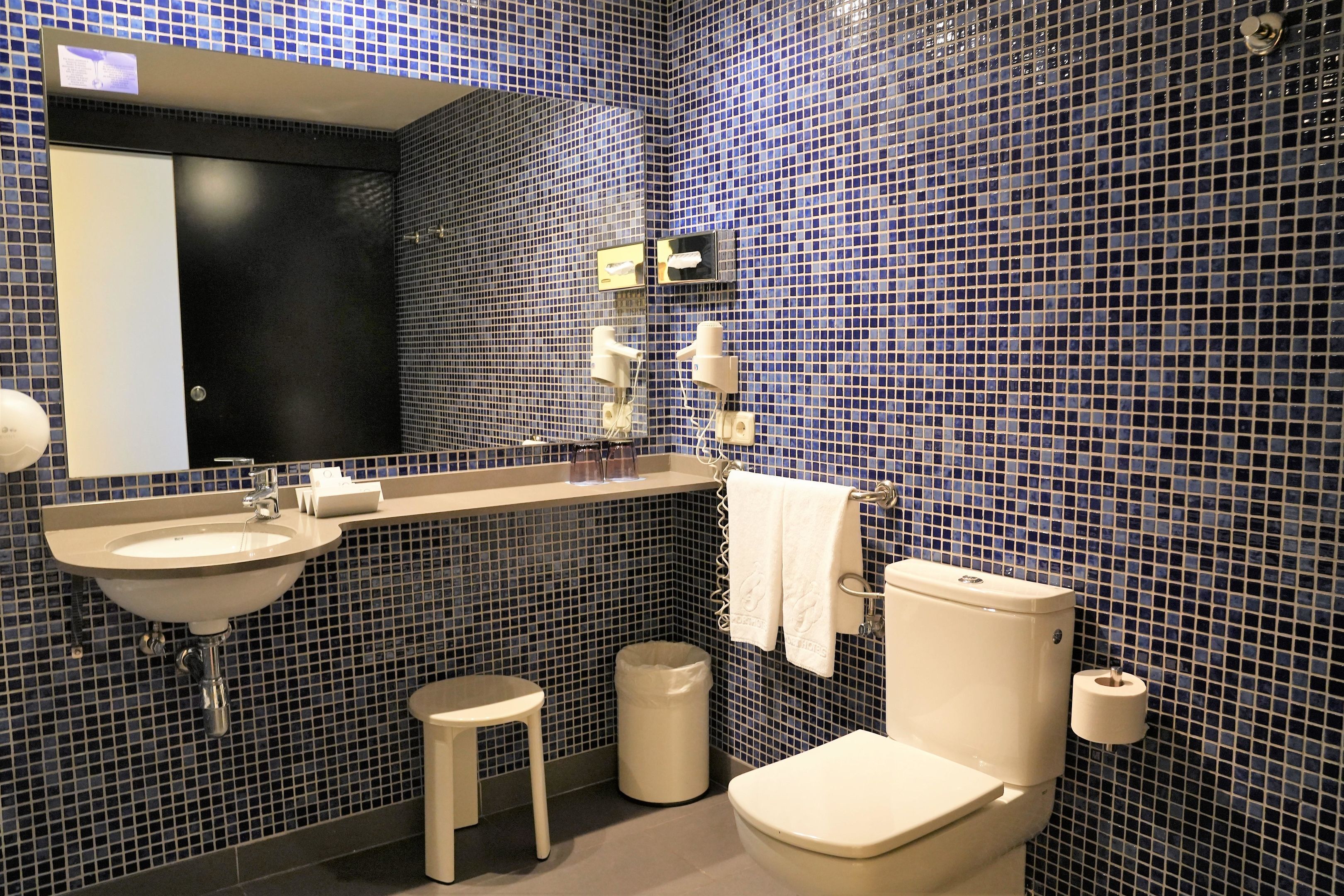 A bathroom with a sink, mirror, toilet, and a trash bin.
