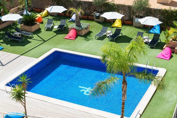 Una piscina con césped artificial, sillas de descanso y sombrillas.