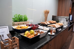 Monipuolinen buffet, jossa on tarjolla erilaisia hedelmiä, leivonnaisia ja juomia.