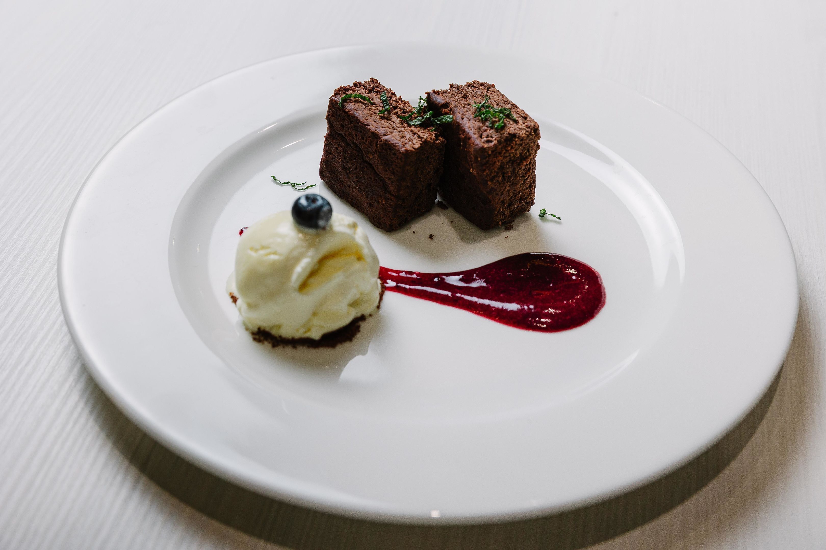 A dessert plate with two chocolate blocks, a scoop of vanilla ice cream, and a red sauce.