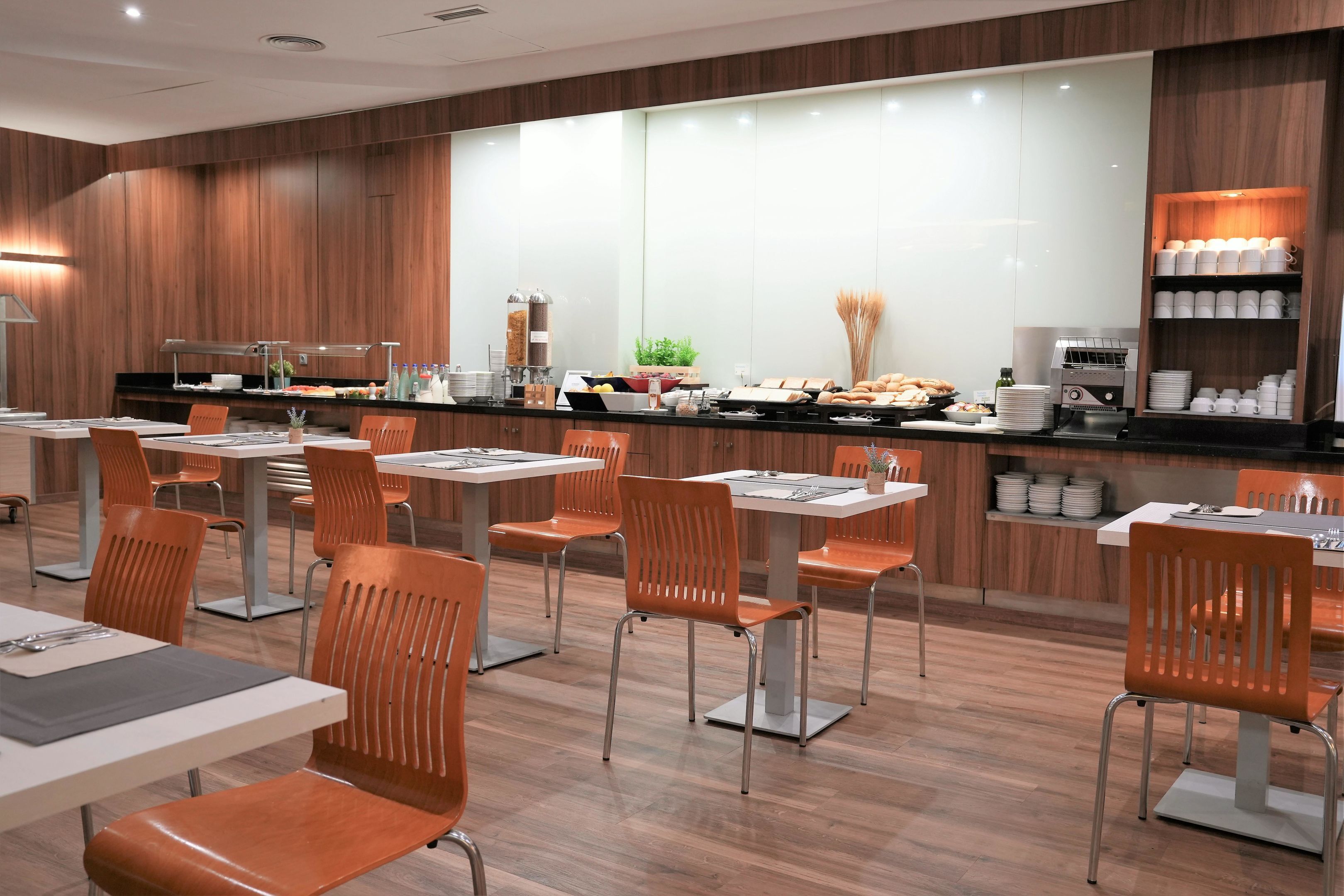 Un comedor moderno con paneles de madera, sillas color naranja y un mostrador tipo buffet con diversos alimentos.