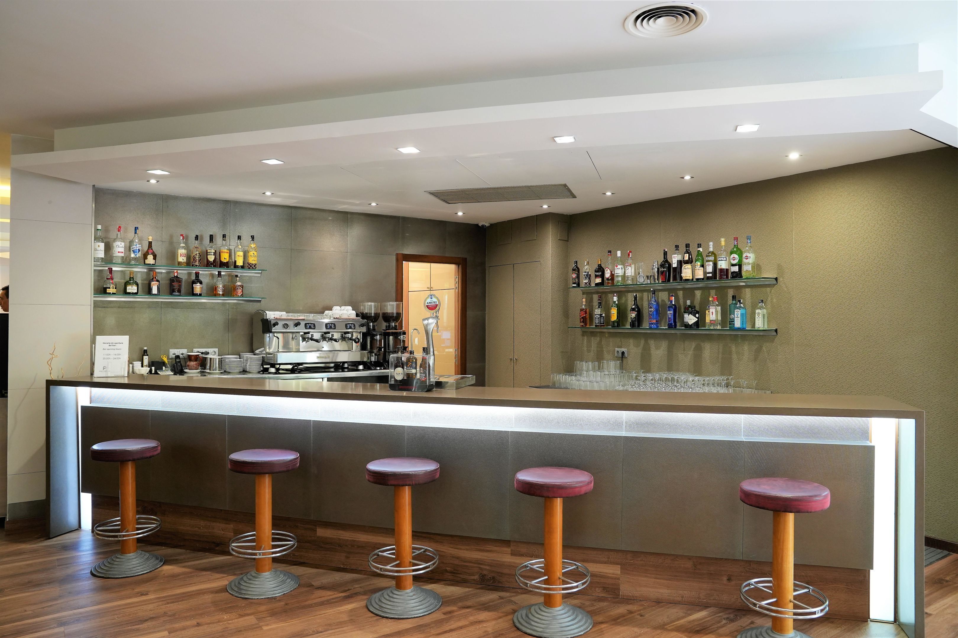 Una zona de bar con taburetes, estantes llenos de botellas y una máquina de café.