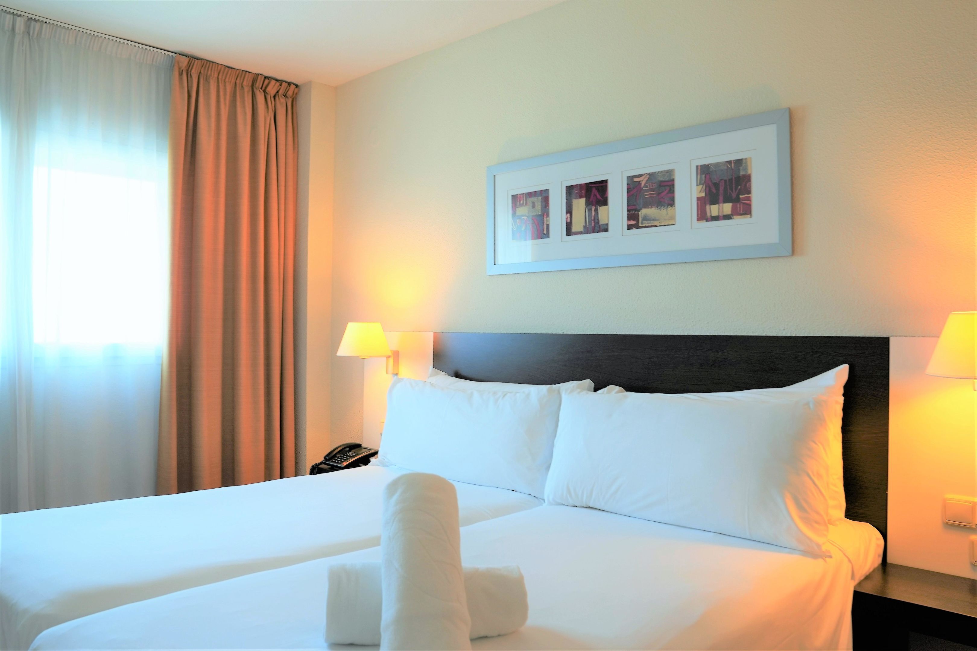 Une chambre d’hôtel avec un lit bien fait, une tête de lit, un tableau encadré au mur et une lampe sur la table de chevet.