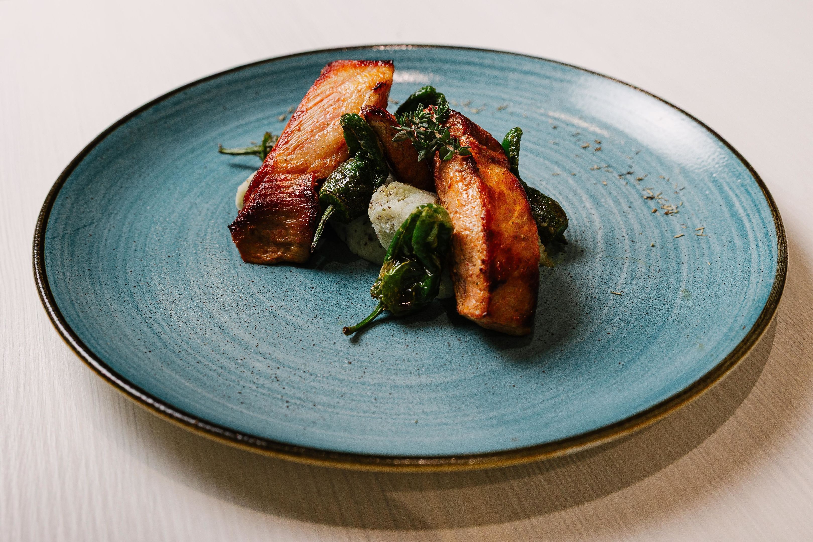 Une assiette contenant divers aliments, notamment du bacon, des asperges et un légume blanc, probablement une pomme de terre, le tout présenté sur une assiette en céramique bleue.