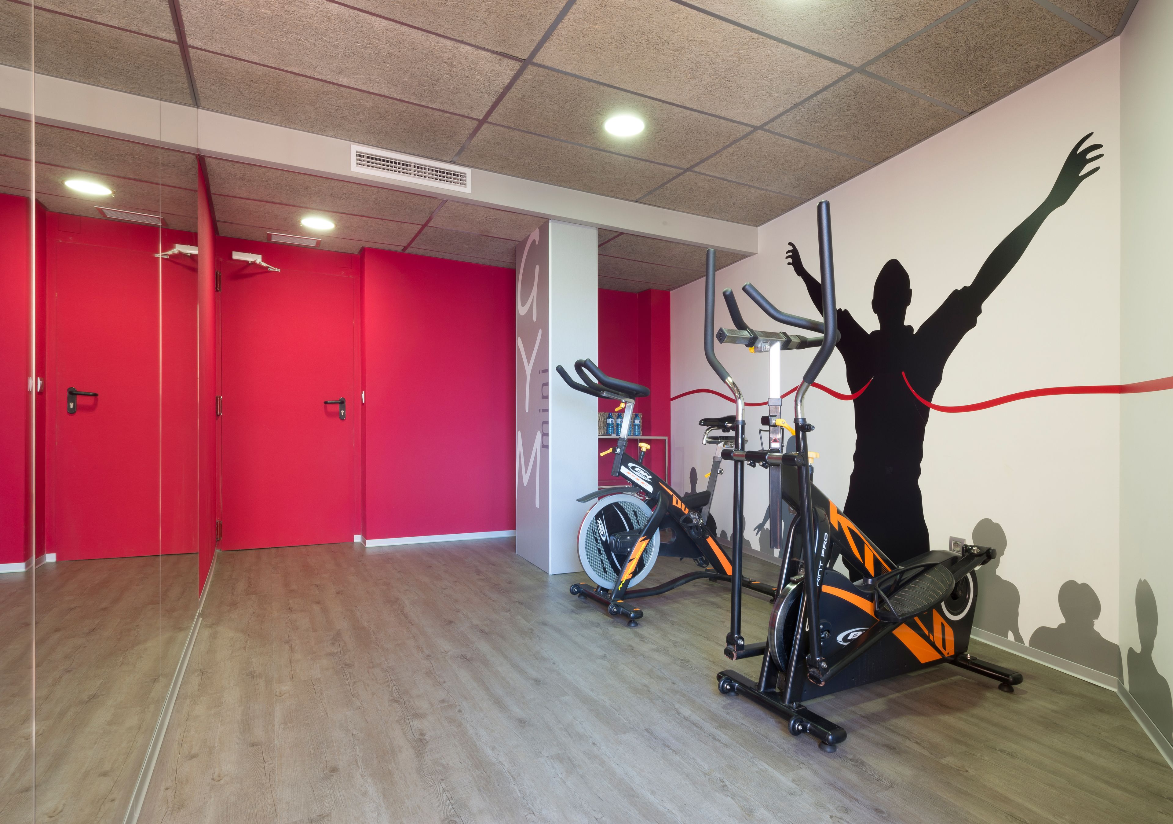 Un gimnasio con paredes rojas, equipamiento de ejercicio y una persona estirándose.