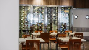 Un restaurante con varias mesas y sillas, una vitrina para vinos y una zona de cocina al fondo.