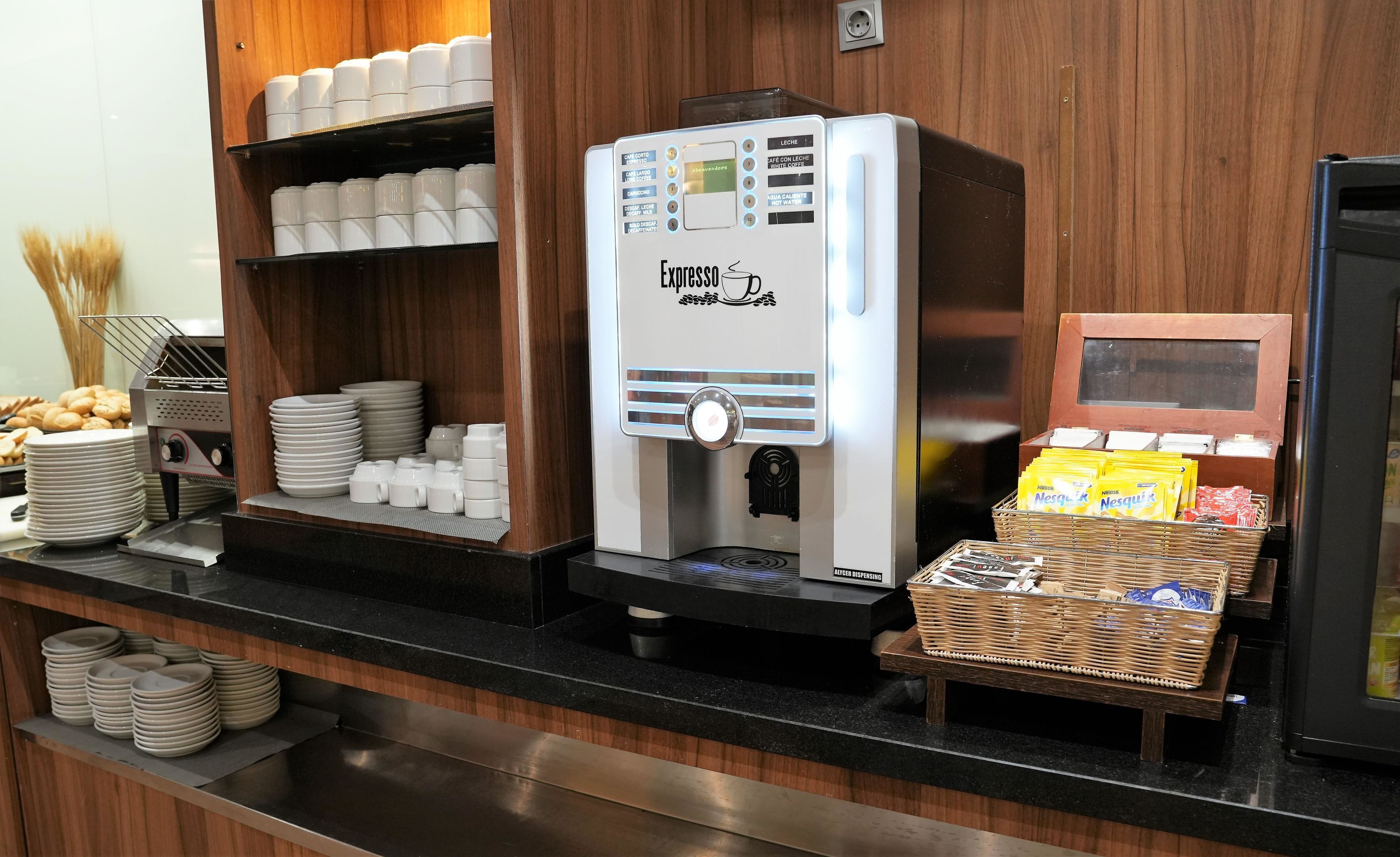 Un angolo caffè con una macchina per espresso, bicchieri usa e getta e un cesto di bicchieri monouso.