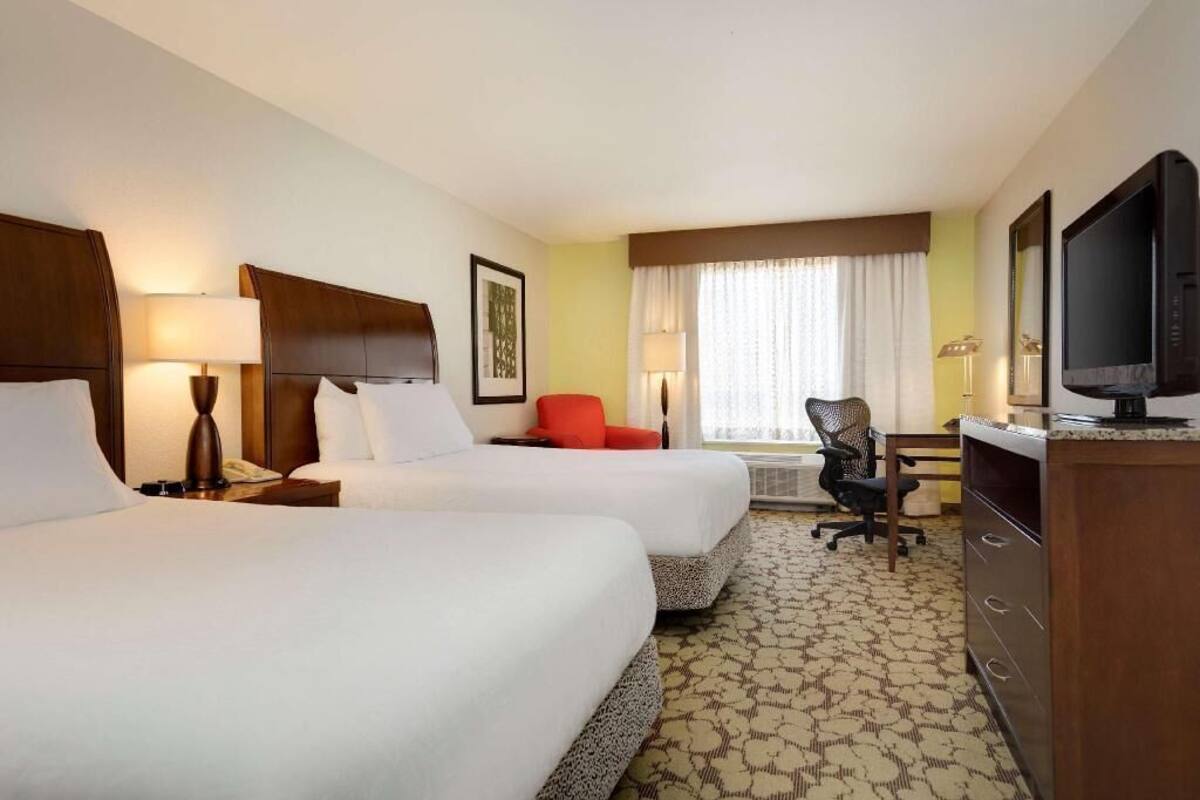 A hotel room with two beds, a desk, a chair, a television, and a window with curtains.