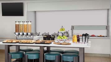 Buffet de café da manhã com diversos alimentos, um espaço para café e assentos com banquinhos.