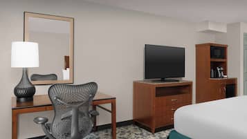 Habitación de hotel con cama, escritorio, silla, televisor, armario y espejo.