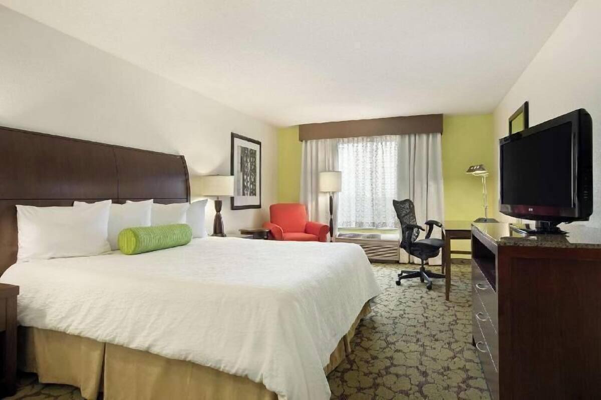 A hotel room with a large bed, a desk with a television, a chair, and a window with curtains.