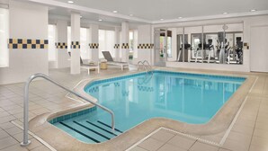 A swimming pool with a tiled deck, a lounge area with chairs, and exercise equipment in the background.